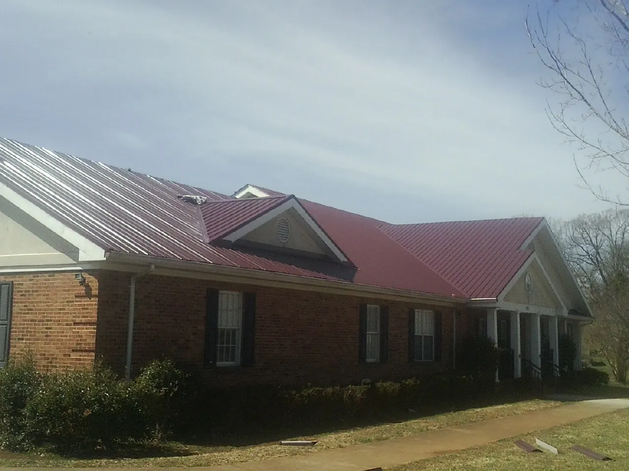 Red metal roof with gabled entries on a long brick building, from a Hail Damage Roof Repair job in Fernley